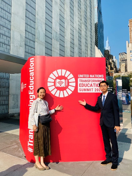 A person and person standing next to a large red bookDescription automatically generated