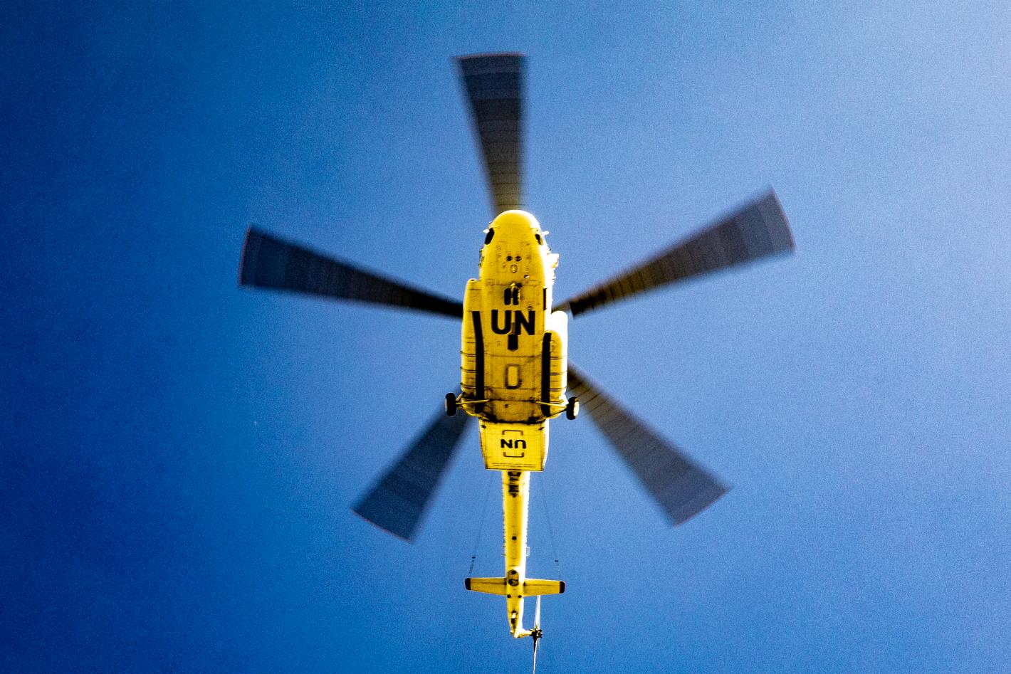 The underside of a yellow UN helicopter against a blue sky