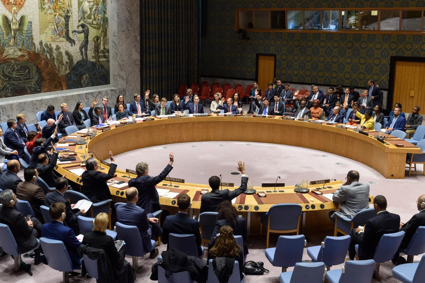 View of the Security Council Chamber with a meeting in session. Several people sitting around the circular table have their hands raised.